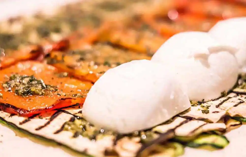 Küchentisch mit Gemüseroulade mit Mozzarella und gebratenem Saibling an Tomaten Kräutervinaigrette.