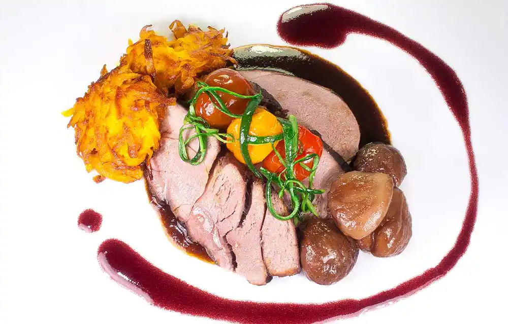 Teller mit Rehschulter in Rotwein geschmort mit Kürbisrösti, Zucchinistreifen und Buttermaroni.