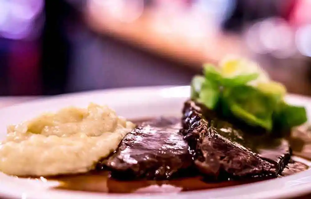 Teller mit Rinderschmorbraten in Rotwein geschmort mit Schwarzwurzelpüree und Rosenkohlblättern.