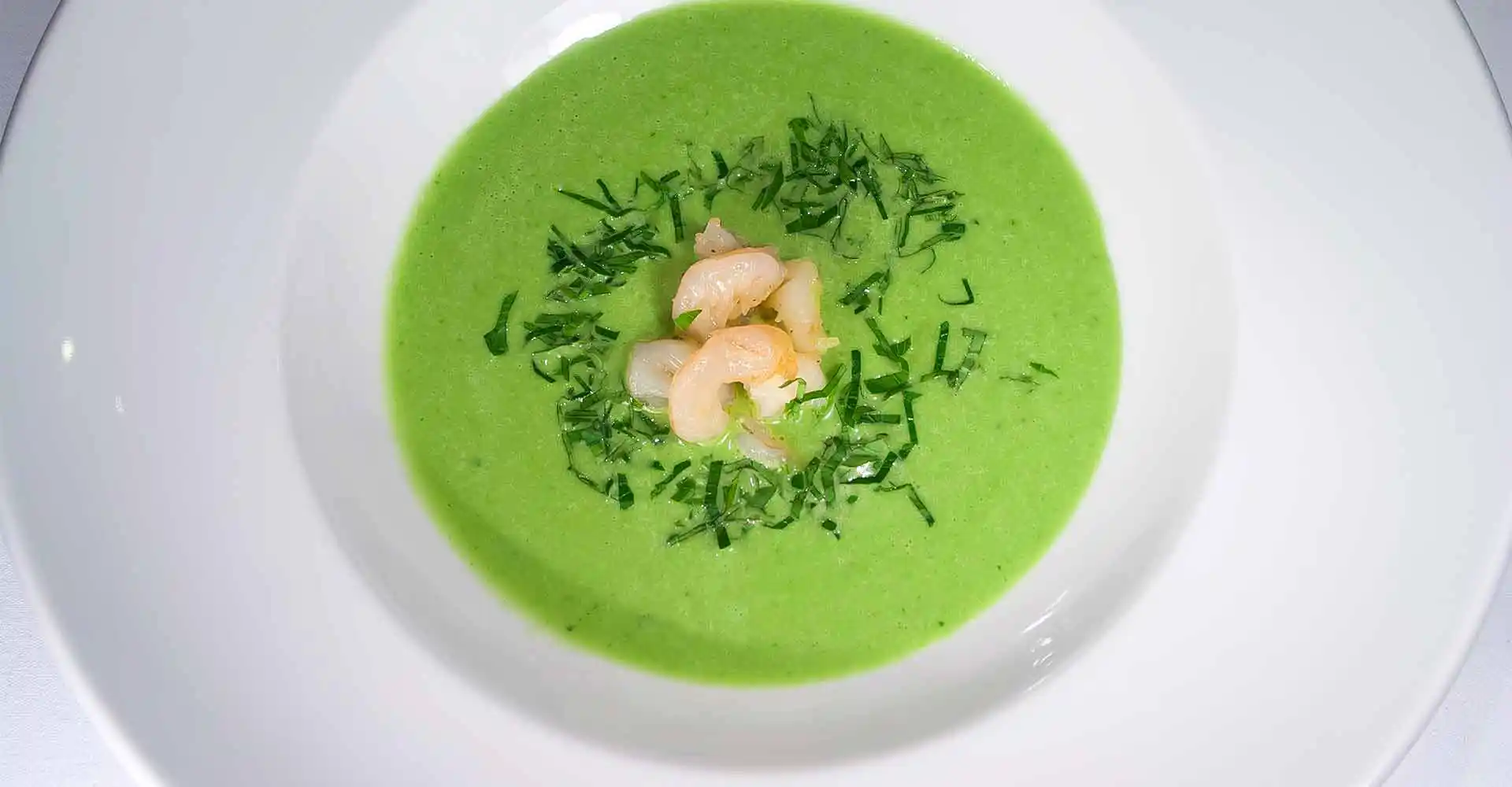 Teller mit Frühlingskräutersuppe und gebratenen Garnelen.