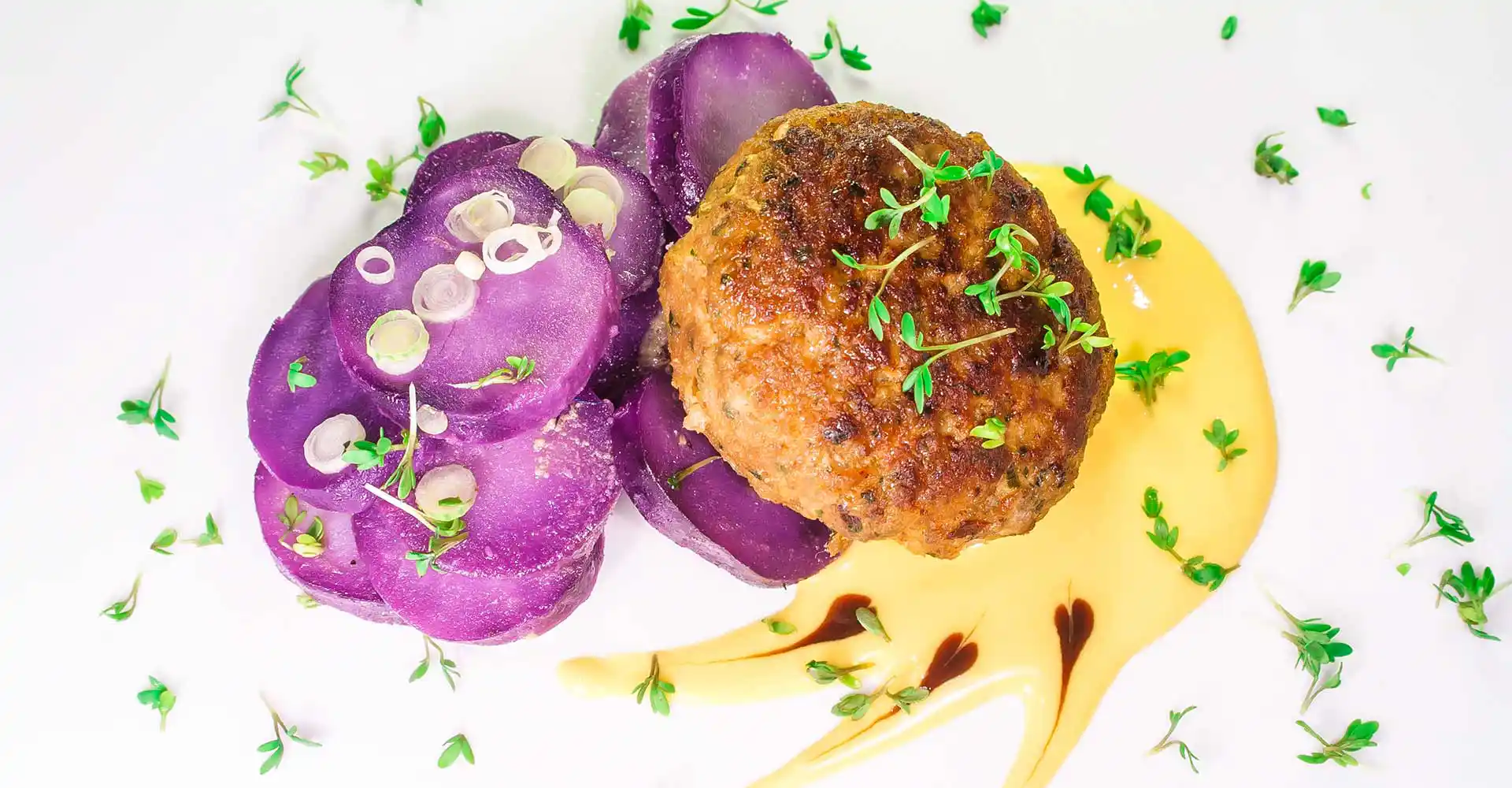 Teller mit Fleischpflanzerl vom Rind und Truthahn an violettem Kartoffelsalat mit Senfcreme.